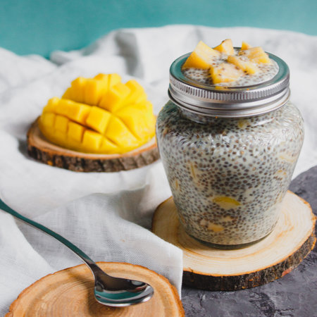 Chia pudding with yellow mango pieces on white linen cloth on turquoise background. Vegan healthy diet conceptの写真素材
