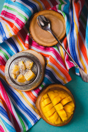Chia pudding with yellow mango pieces on background of clorful striped kitchen cloth. Vegan healthy...