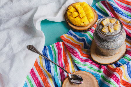 Chia pudding with yellow mango pieces on background of clorful striped kitchen cloth. Vegan healthy diet conceptの写真素材