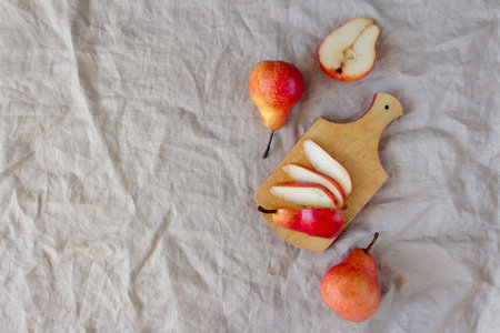 Overhead bright red williams pears on linen wrimkled textile background. Sliced fruit on small...