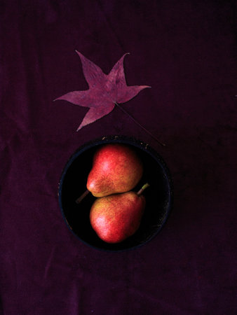 Two bright red williams pears in wooden bowl and maple autumn leaf on burgundy velvet background. Overhead minimal still life.の写真素材
