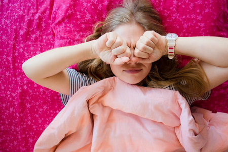 Overhead portrait of unhappy woman hiding her eyes by hands sleeping in bed with a bright pink...