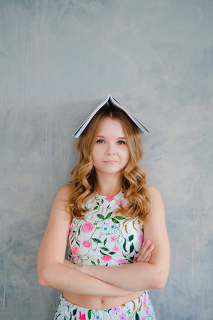 Pretty young woman holding an open book on her head like a roof. Cute and funny education concept