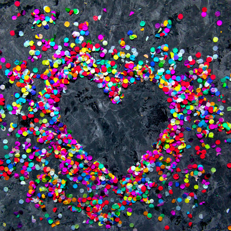 Frame in shape of heart made of colorful confetti on black textured background.の写真素材