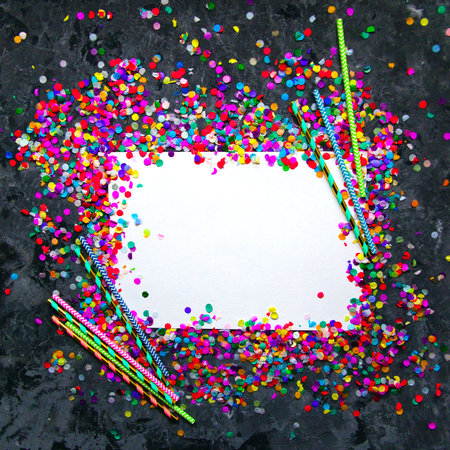 White sheet of paper in frame made of colorful confetti and straws on black textured background.の写真素材