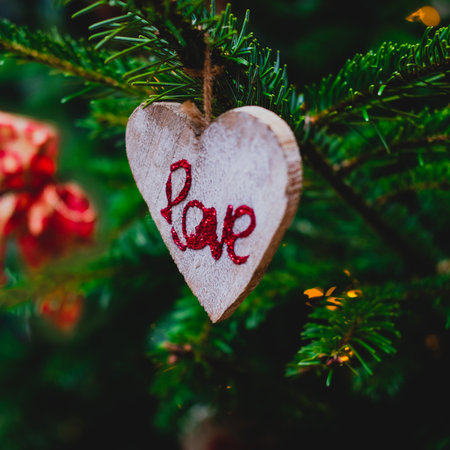 Word love written with red glitter on wooden decorations in shape of heart hanging on a pine branch on Christmas tree. Romantic holiday concept.の写真素材