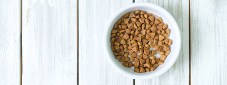 Dry cats food in a round bowl on white wooden floor overhead.の写真素材