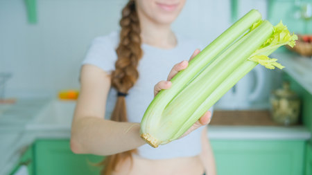 Woman holding celery stalk in stylish minimal kitchen. Healthy lifestyle conceptの写真素材