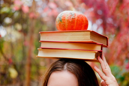 Stack of three vintage paper books and a small cute pumpkin on female head. What to read in autumn concept.の写真素材