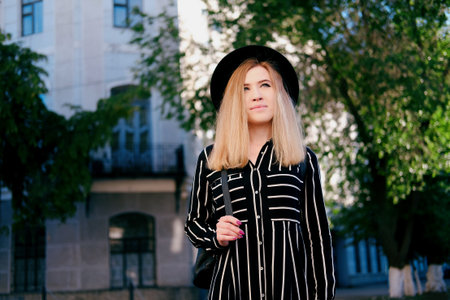 Blonde girl in black hat walking on the street. City traveling alone concept.の写真素材