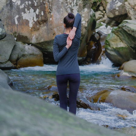 Young slim woman practicing yoga outdoors on stone shore of mountain river. Unity with nature...