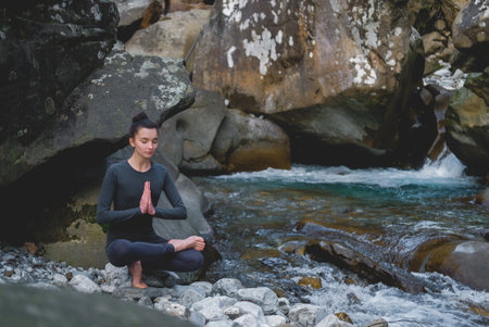 Young slim woman practicing yoga outdoors on stone shore of mountain river. Unity with nature concept. Girl sitting on tiptoes.の写真素材