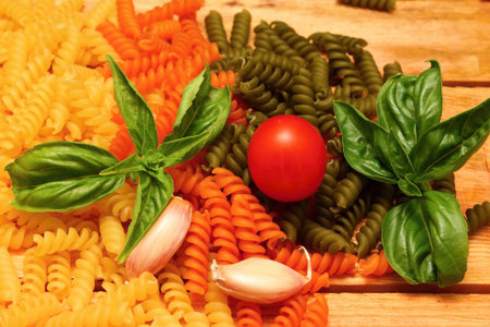 Wooden table with different kinds of colored pasta and vegetableの写真素材
