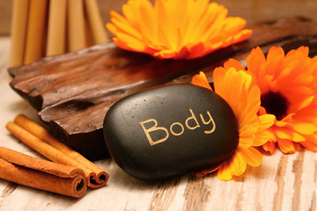 Black lava stones and marigold flower blooms on wooden boards with cinnamon and bamboo in backgroundの写真素材