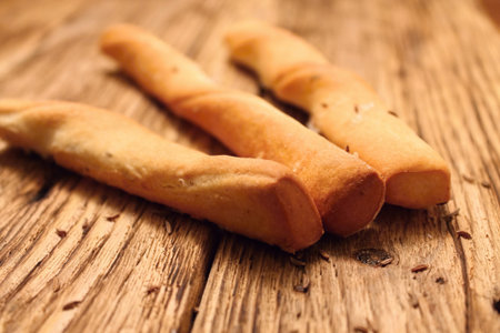 Three sesame sticks placed on old wooden board with cumin seeds aroundの写真素材