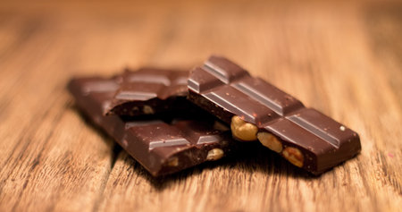 Photo of three pieces of chocolate with hazelnuts inside placed in the middle of old worn wooden board with very deep grooves. Chocolate is blurred by camera.の写真素材