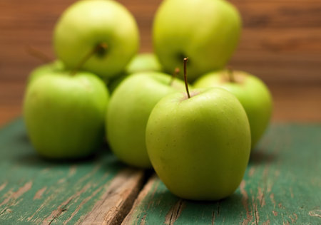 Photo of heap of green apples with one in front which is sharp. All are placed on old wooden board with significant grooves.の写真素材