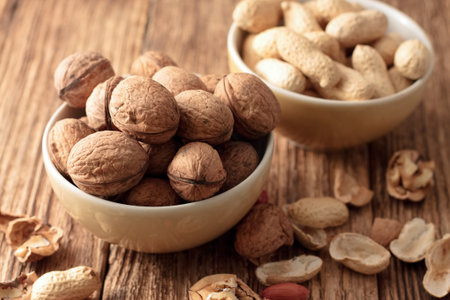 Photo of two bowls, one with walnuts and second with peanuts placed on old worn wooden table with...