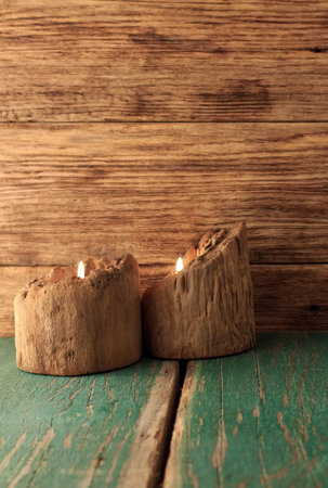 Vertical photo of two candlesticks made from wooden bars placed on wood board with worn green color and with wooden bars in backgroundの写真素材