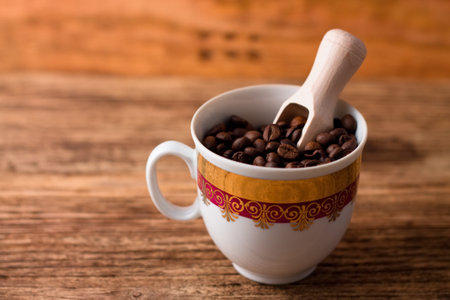Photo of Cup full of coffee grains and wooden spoon inside placed on old wooden board.の写真素材