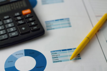 Horizontal photo of yellow pen placed on paper sheets with blue pie charts with black calculator in...