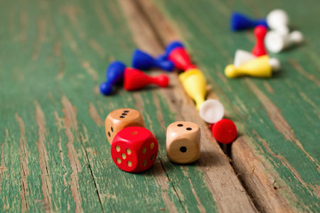 Horizontal photo of Few dices and color figurines for ludo placed on old wooden board with worn...