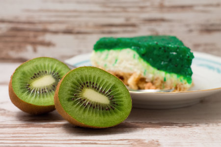 Horizontal photo of Kiwi fruit cut in half on white board in front of green cake which is placed on white plate with light blue ornamentの写真素材
