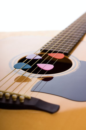 Vertical photo of front side of acoustic guitar with bridge, strings and fretboard. Four colorful guitar picks are placed in strings over the hole in spruce board.の写真素材
