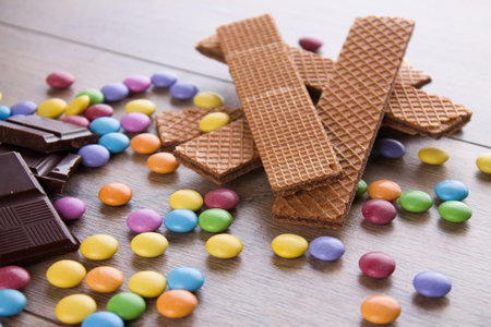 Horizontal photo of few chocolate biscuits on wooden board with colorful chocolate sweet smarties around. Pieces of chocolate are placed on border.の写真素材