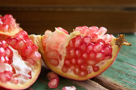 Horizontal photo of single pomegranate divided to three parts with visible pink seeds. Fruit is on green worn wooden board in front of old books.の写真素材