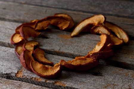 Vertical photo of heart shape consists of pieces of dried apple. Shape is placed on old wooden board with grey color.の写真素材