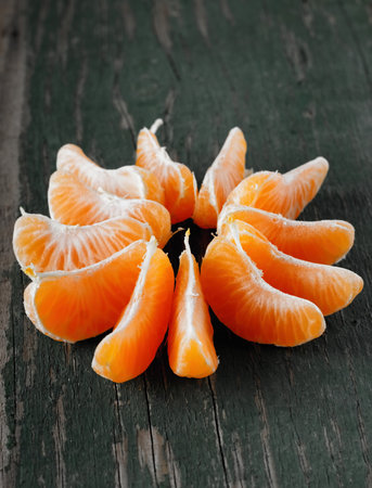 Vertical photo with single mandarin divided to pieces into a shape of orange star. Fruit is placed on very old wooden board with worn green color.