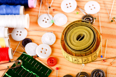 Horizontal photo with tailoring accessories placed on light wooden color like color pins, tape measure, several knobs, needles and sewing.の写真素材
