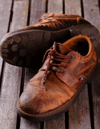 Vertical photo of two very old worn shoes with damaged surface and shoelaces. One boot has visible...