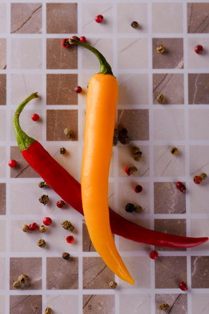 Vertical photo of two chili peppers with yellow and red color which are placed on ceramic tile. Vegetable has several color pepper seeds around.の写真素材
