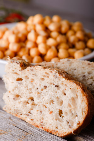 Vertical photo of two slices of wholewheat bread in front of white bowl full of orange chickpeas vegetable. Red cherry tomatoes are next to bowl on wooden board.の写真素材
