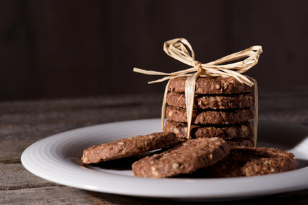 Horizontal photo of white plate placed on wooden board with few brown cereal biscuits. Few biscuits...