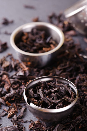 Vertical photo of metal tea strainer which is divided to two three parts. Dry tea leaves are in strainer and spilled around on black slate stone which is used as a plate.の写真素材