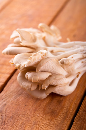 Vertical photo of fresh bunch of oyster mushroom. Healthy foodstuff placed on wooden board with brown color made from planks. Table with nice textured surface.の写真素材