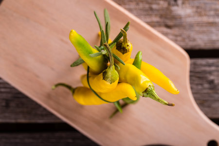 Horizontal photo with top view on bunch of green and yellow chili peppers together with sprig of rosemary herb bonded by chive. Vegetable stands on tops on chopping board.の写真素材