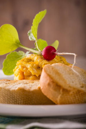 Vertical photo of single portion of yellow scrambled eggs. Eggs in shape of tower. Single small red raw radish with leaves. Couple of roasted pastry on white plate with dark sauce.の写真素材