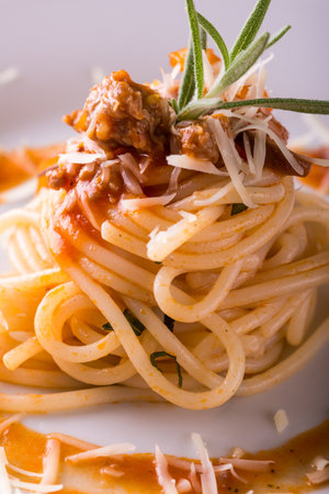 Vertical photo of single portion of spaghetti pasta food. Orange sauce is on food and spilled around on plate. Cheese pieces are on and around. Minced meat is on the top with rosemary herb.の写真素材