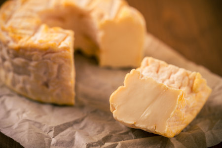 Horizontal photo of whole special camembert cheese with golden color and hole in the middle with cut off single portion. Cheese is placed on crumpled paper and dark wooden board.の写真素材