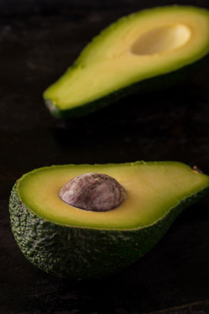 Vertical photo of single green raw severed avocado which is cut to two halves. Both pieces are...