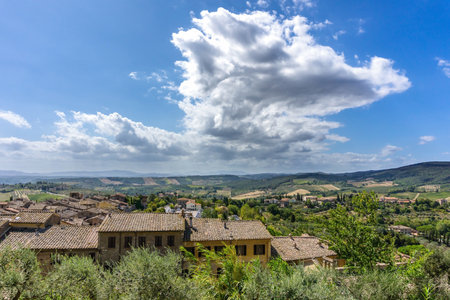 Horizontal photo with few rustic houses which are built on side of historic town in Tuscany Italy. The landscape with hills, rocks, olive trees and forests is in background. Sky is cloudy.の写真素材