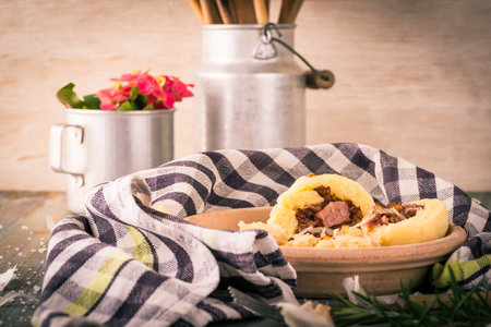 Horizontal photo of potato dumplings filled by smoked pork meat. Sour cabbage with fried onion is next to meal on clay plate with towel placed on wooden board with metal cups, garlic and rosemary.の写真素材