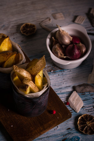 Vertical photo with almost top view on vintage cans with fried potatoes. Vegetable was roasted with skin. Cans are on chopping board and table with worn blue color.の写真素材