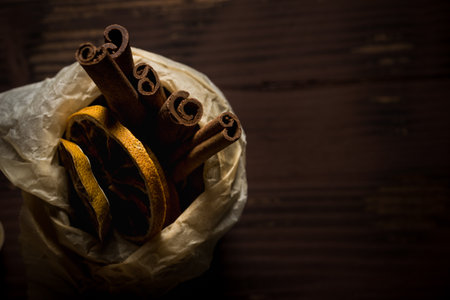 Horizontal photo with top view on vintage can filled by paper. Inside are few pieces of cinnamon sticks and dry orange rings. All is placed on dark brown vintage wooden board.の写真素材