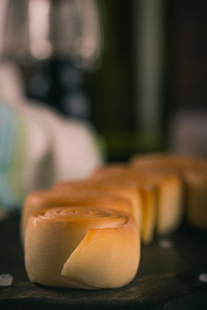 Vertical photo with few cheese rolls in a row. Rolls of smoked cheese parenica are placed on dark rustic wooden board with spice and salt spilled around. Green white towel is in background.の写真素材