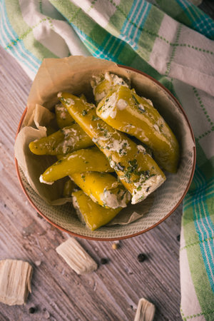 Vertical photo with top view on ceramic bowl full of hot green peppers. Vegetable is stuffed by cream cheese with spicy herbs. White checkered towel is next to bowl on wooden board.の写真素材